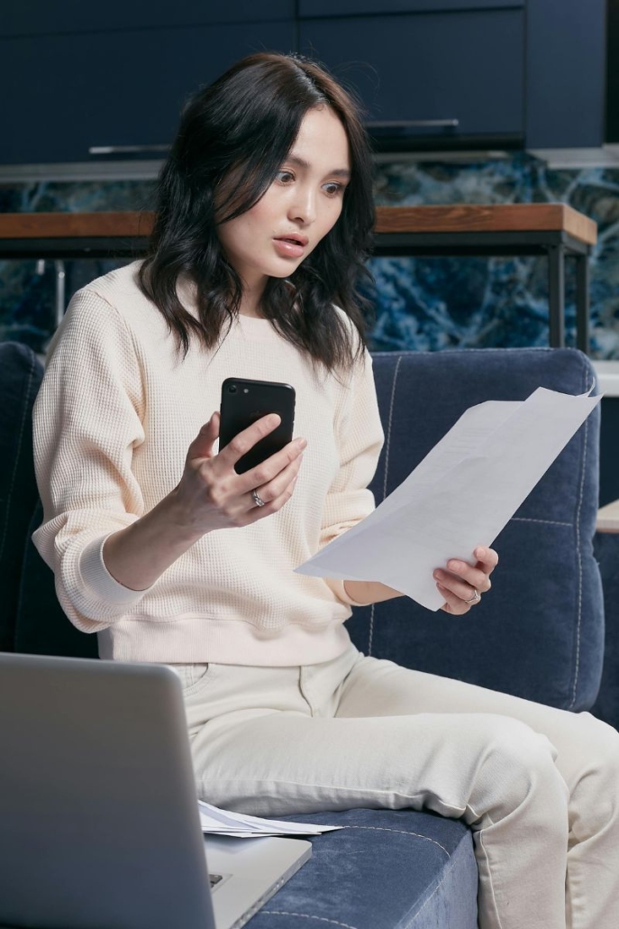 Woman holding cell phone and looking at a bill with shock